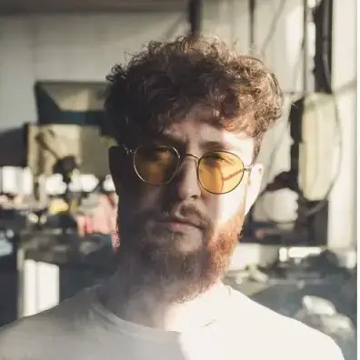 Young man with dark hair and beard, brown eyes, blue t-shirt