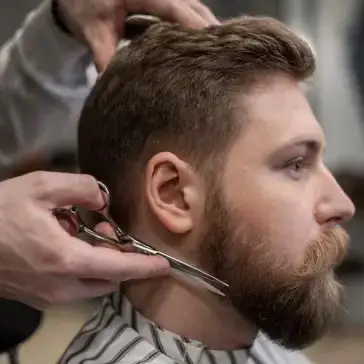 young man side profile having beard trimmed with scissors